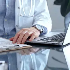 Lekarz rodzinny wypisuje receptę na depresję. Na biurku leży laptop i dokumenty.