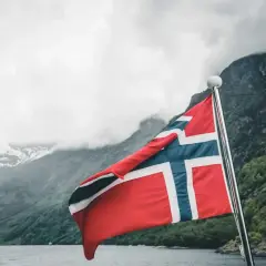 Norweska flaga na tle fiordu. Marzenie o wysokich zarobkach w Norwegii staje się bliższe.