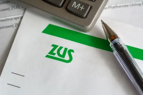 Długopis i kalkulator leżą na papierze z logo ZUS. Czas na rozliczenie składek społecznych.