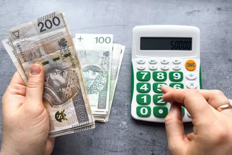 Dłoń trzyma banknoty 200 zł i 100 zł, obok kalkulator z wyświetloną kwotą 50000. Czy to najniższa brutto?
