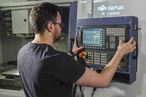 Operator CNC przy panelu sterowania maszyny. Zastanawiasz się, ile zarabia operator CNC w Niemczech?