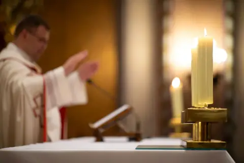 Ksiądz w kościele podczas mszy, zapalone świece. Czy księża płacą podatki? To pytanie nurtuje wielu.