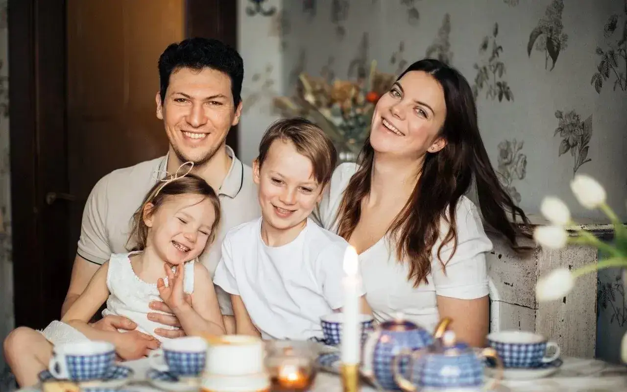 Rodzina przy stole, dzieci śmieją się radośnie. Kindergeld i praca dziecka to temat, który może być poruszany w takiej rodzinnej atmosferze.