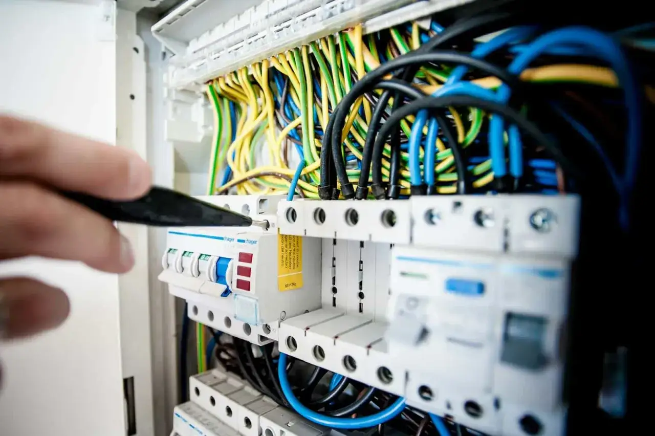 Ręka majstruje przy skrzynce z bezpiecznikami, tworząc ścieżkę do dobrze płatnej pracy dla elektryka.