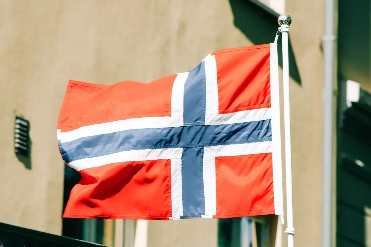 Norweska flaga powiewa na wietrze, symbolizując marzenia o wysokich zarobkach w Norwegii.