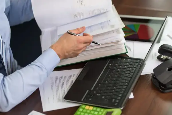 Osoba przegląda dokumenty, na biurku laptop, kalkulator i wykres kołowy. To może być pomocne przy wypełnianiu karty podatkowej.