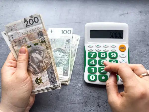 Dłoń trzyma banknoty 200 zł i 100 zł, obok kalkulator z wyświetloną kwotą 50000. Czy to najniższa brutto?