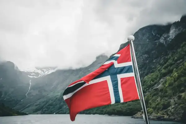 Norweska flaga na tle fiordu. Marzenie o wysokich zarobkach w Norwegii staje się bliższe.